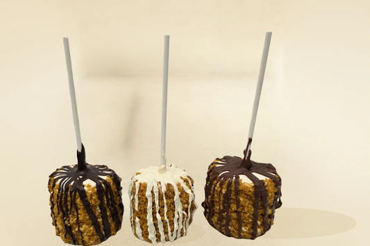 Three toffee marshmallow pops on sticks with different toppings against a beige background