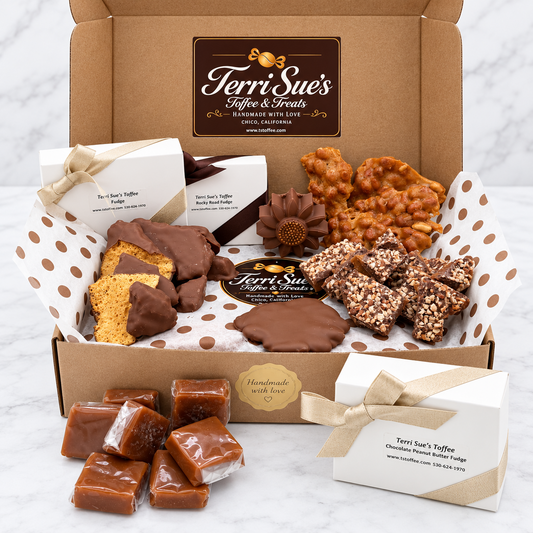 An open cardboard gift box filled with assorted chocolate treats and sweets, arranged on white tissue paper with brown polka dots. Visible products include chocolate-dipped cookies, chocolate-covered pieces, caramel squares, and boxed chocolates.