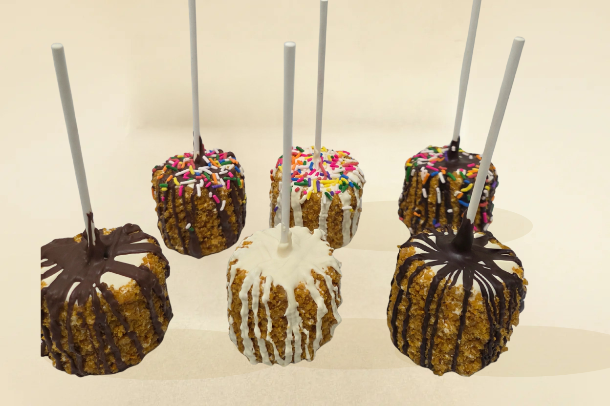 Caramel apples with various toppings on sticks against a beige background