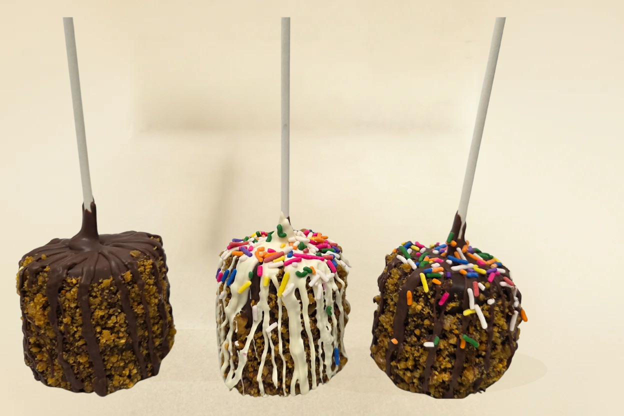 Three toffee marshmallow pops with different toppings on a beige background